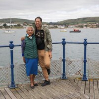 Two participants hugging as they lean against the railings, with the sea and boats in the background.