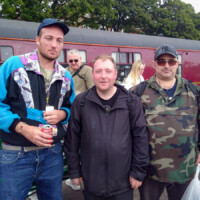 Three participants smiling at the camera as they stand in front of a train.
