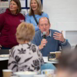 A trustee holding a microphone, sat at a table, talking about his experience with Fair Shares.