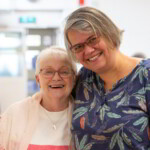 Two participants smiling at the camera, one with their arm over the shoulder of the other.