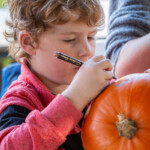 Young boy looking focused as he draws a design on a pumpkin.
