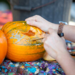 Close up of a person using a knife to carve out a mouth on a pumpkin. The eyes are already carved.