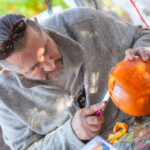A man holding a pumpkin steady with one hand and using a knife in the other to carve a design into it.