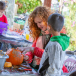 Katie helping carve out a design on a pumpkin for a young boy stood next to her.