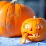 Two pumpkins, one in the background uncarved and the one in the foreground with a face carved into it.