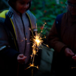 A child in a coat holding a sparkler which is about half way done.
