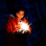 A yong child in a red coat, holding a sparkler.