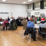 A wide shot of the hall, full of tables with participants sat around them.