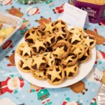 A plate full of mince pies surrounded by plates with other snacks on.