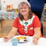 Gill, sat at a table with a santa hat on and a plate full of food.