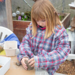 A young girl in an oversized shirt playing with clay.