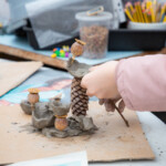 Close up of a child using clay to make a figurine with seed pods and pinecones.