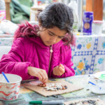 A young girl in a pink coat putting multicoloured beans on a snail template.