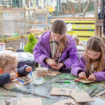 Three kids sat around a table, glueing beans onto animal templates.