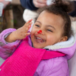 A child giggling with paint on their fingers and the tip of their nose.