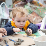 A small child using a clay tool to sculpt some clay.