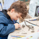 A young boy using a clay knife to sculpt some clay for his scorpion.