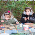 Two young girls. One of putting glue on her template of a butterfly. The other is using a felt tip to decorate her butterfly.
