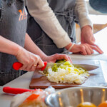 Close up photo of a person using a knife to dice spring onions.