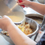 Close up shot of someone pouring a liquid mixture into a bowl full of torn up danish pastries.