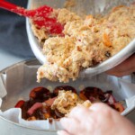 A close up shot of a cake mixture being poured from a metal bowl into a cake tin lined with parchment.