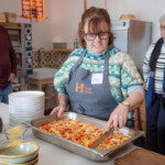Jane is using a knife to slice up the quiche as members of the group look on.