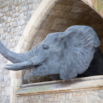 Sculpture of an elephant sticking it's head out from the wall, made out of metal.