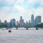 A photo taken on the Thames showing all of the London high-rise buildings and a glimpse of the Houses of Parliament.