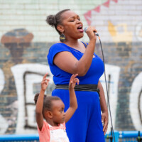 A woman singing karaoke at the 2024 cultural fayre, and her child dancing alongside her.