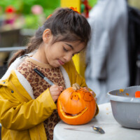 A child in a yellow jacket concentrating as she draws a design onto her pumpkin.