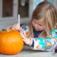 Child drawing a design onto their pumpkin.