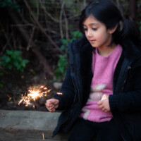 A child sat on a bench watching their lit sparkler.