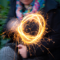 Long exposure of an adult sat on a bench, making circles with their lit sparkler.