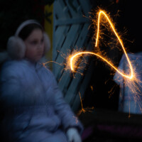 A long exposure of a girl sat down, playing with her sparkler.