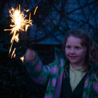 A child smiling as she watches her lit sparkler.